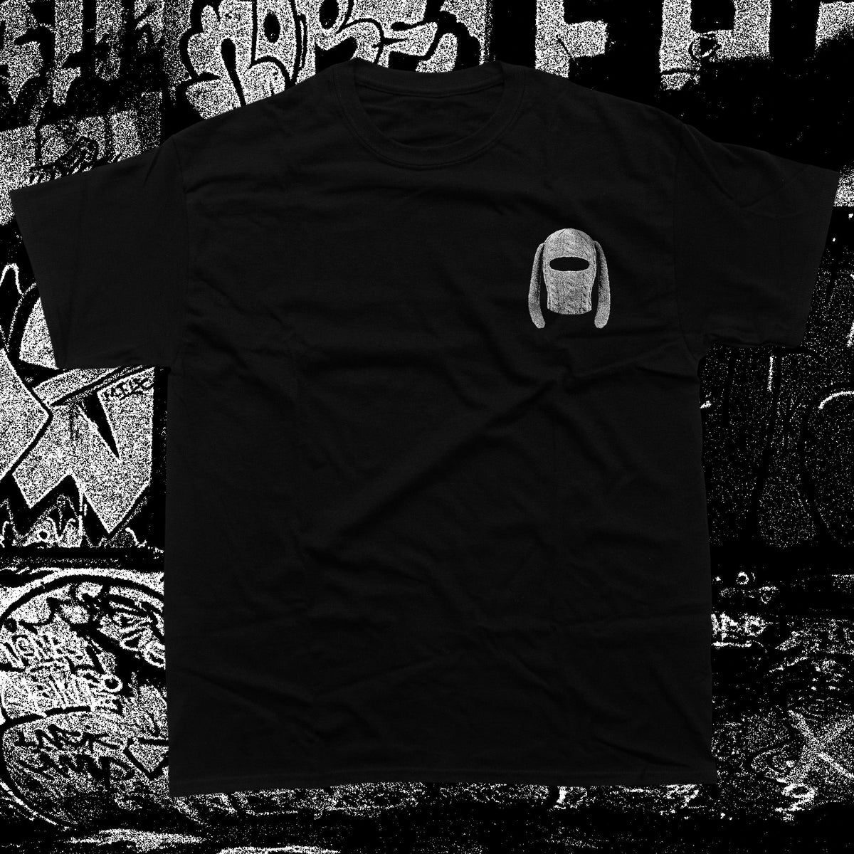 A black short-sleeve t-shirt with a small gray graphic of a hooded figure on the left chest, displayed against a black and white graffiti-covered background.